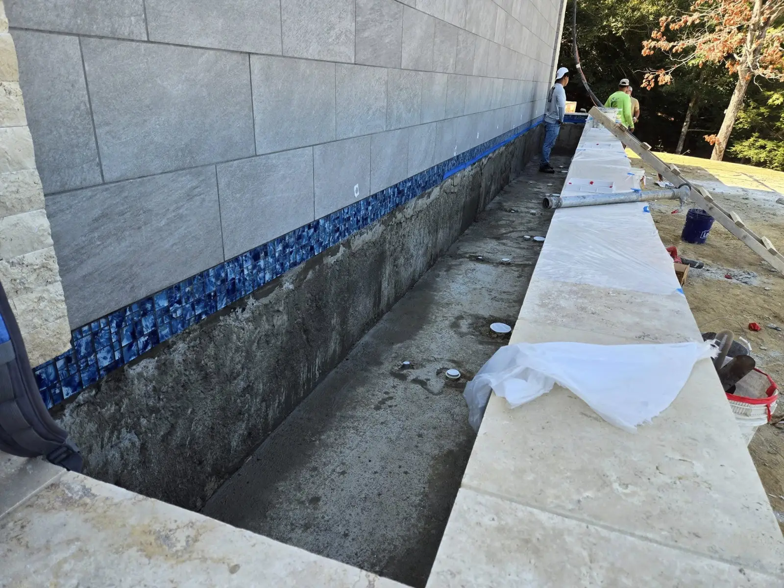 Glass waterline tile and travertine coping being installed